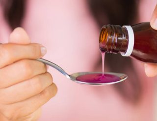 Woman hand pouring medication or antipyretic syrup from bottle to spoon. healthcare, people and medicine concept.